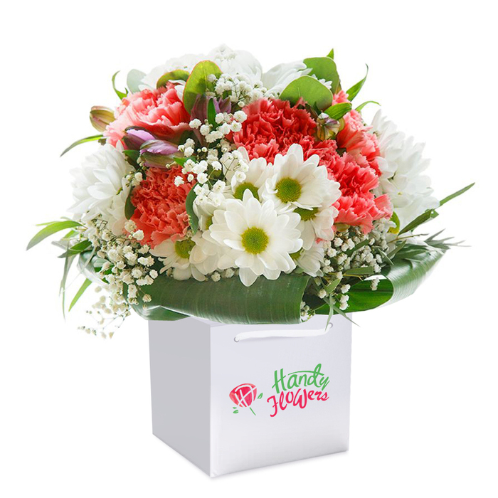 Within a smart white gift bag set against a minimalist white backdrop, this beautifully constructed Berrylands bouquet captures the neighbourly warmth and natural appeal of its locale. The starring carnations unfurl in hues of coral, subtle peach, and vibrant red, their sumptuous ruffled petals gathered in generous profusion. Dotted among them, pure white daisies with vibrant chartreuse centers evoke the brightness of a sunny day in Alexandra Park or along Tolworth Rise. Wispy clouds of baby's breath thread through the floral display, imparting a dreamlike delicacy that softens the whole composition. Rounding out the bouquet, glossy, dark green foliage and broad leaf shapes frame the flowers, offering a harmonious reference to the abundant greenery of Berrylands' gardens. Suspended within the ensemble, a few closed purple-tipped buds suggest the anticipation of new beginnings. The arrangement sits neatly in a square white bag, thoughtfully designed with crisp ribbon handles for easy portability to homes or celebrations throughout KT5. Every bloom within this hand-tied bouquet has been positioned for maximum impact and freshness, a testament to the professional touch of Berrylands Flowers. The final image, carefully lit and composed, showcases both the technical skill and heartfelt artistry of local florists, making it an inspired choice for birthdays, anniversaries, or just-because gifts delivered to friends and family across Berrylands.